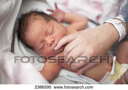 Stock Photography - Newborn baby with eyes closed sucking on mother's pinky finger; Toronto, Ontario, Canada. Fotosearch