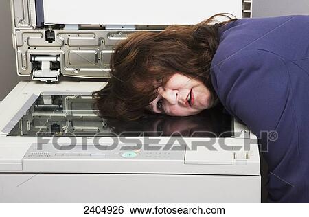 Stock Photograph - Office worker putting head in photocopier out of frustration; Edmonton, Alberta, Canada. Fotosearch