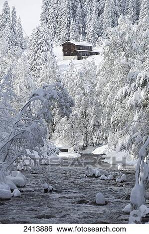 Stock Photograph - Open creek along snow covered banks with snow covered trees, house and mountain slope in background; Hintertux, Austria. Fotosearch