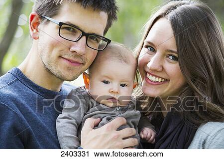 Stock Image - Portrait of a married couple with infant daughter in a park; Edmonton, Alberta, Canada. Fotosearch