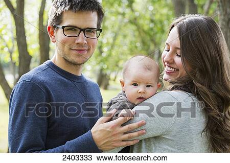 Stock Image - Portrait of a married couple with infant daughter in a park; Edmonton, Alberta, Canada. Fotosearch