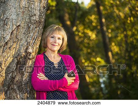 Stock Photo - Portrait of a woman in a park holding her cell phone; Edmonton, Alberta, Canada. Fotosearch