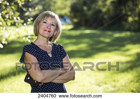 Stock Image - Portrait of a woman standing in a park holding her cell phone; Edmonton, Alberta, Canada. Fotosearch