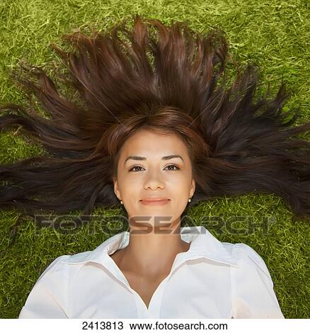 Stock Image - Portrait of a young woman laying on the grass with her long hair fanned out around her; Edmonton, Alberta, Canada. Fotosearch