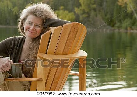 Portrait Of Smiling Woman Seated Sideways In Deck Chair Holding Mug, Clear Lake, Manitoba, Canada View Large Photo Image Stock Image - Portrait Of Smiling Woman Seated Sideways In Deck Chair Holding Mug, Clear Lake, Manitoba, Canada. Fotosearch