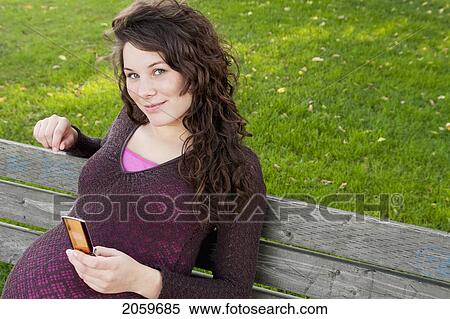Pregnant Woman On Park Bench Holding Cell Phone, Manitoba, Canada View Large Photo Image Stock Photography - Pregnant Woman On Park Bench Holding Cell Phone, Manitoba, Canada. Fotosearch
