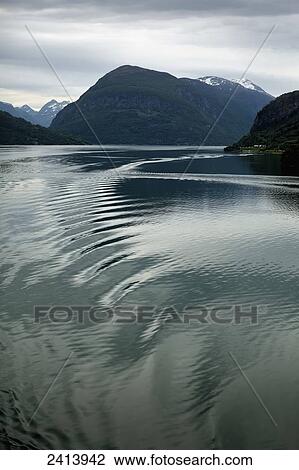 Stock Image - Ripples in the water reflecting cloud with mountains along the shoreline in the distance; Olden, Norway. Fotosearch