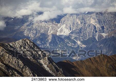 Rugged mountain peak with sun lit mountain range in the distance with cloud covering the peaks; Hinterux, Austria View Large Photo Image Stock Image - Rugged mountain peak with sun lit mountain range in the distance with cloud covering the peaks; Hinterux, Austria. Fotosearch