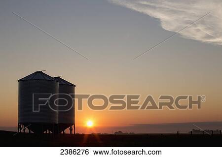 Silhouette of two metal grain bins at sunrise with orange sun and blue sky; Airdrie, Alberta, Canada View Large Photo Image Stock Photograph - Silhouette of two metal grain bins at sunrise with orange sun and blue sky; Airdrie, Alberta, Canada. Fotosearch