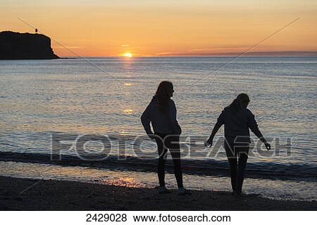 Silhouette of two young women on a beach at the water's edge at sunset; Trout River, Newfoundland, Canada View Large Photo Image Stock Photo - Silhouette of two young women on a beach at the water's edge at sunset; Trout River, Newfoundland, Canada. Fotosearch