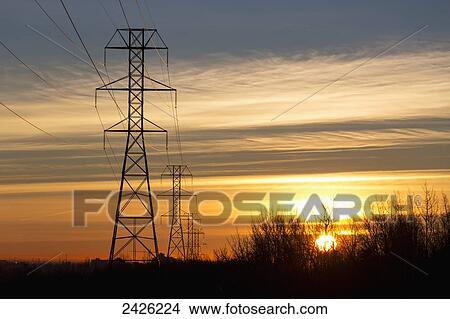 Silhouetted electric towers with wires at sunrise with orange cast clouds and blue sky; Calgary, Alberta, Canada View Large Photo Image Picture - Silhouetted electric towers with wires at sunrise with orange cast clouds and blue sky; Calgary, Alberta, Canada. Fotosearch