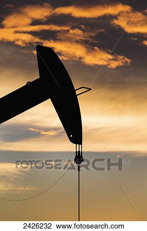 Stock Image - Silhouetted pumpjack head at sunset with orange cast clouds; Alberta, Canada. Fotosearch