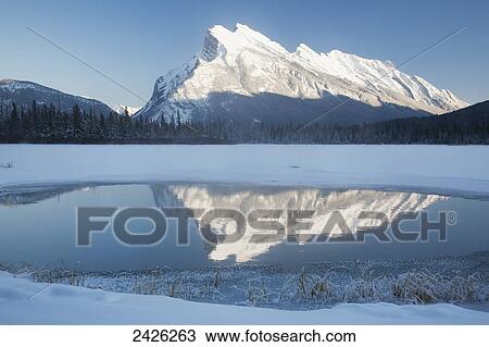 Snow covered mountain reflecting in open water on a snow covered lake and blue sky; Banff, Alberta, Canada View Large Photo Image Stock Image - Snow covered mountain reflecting in open water on a snow covered lake and blue sky; Banff, Alberta, Canada. Fotosearch