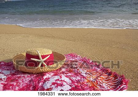 Stock Image - Straw Hat With Dark Pink Band And Seastar On Dark Pink And White Batik Pareo (Sarong), Beach, Ocean And Sky Background.. Fotosearch