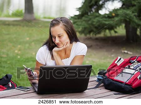 Stock Image - Student listening to music while studying outdoors using a laptop; St. Albert, Alberta, Canada. Fotosearch