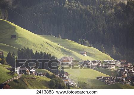 Stock Image - Sun lit rolling grassing slopes with alpine houses and barns; Lanserbach, Austria. Fotosearch