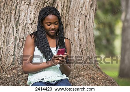 Stock Image - Teenage girl using a smart phone in a park; Edmonton, Alberta, Canada. Fotosearch