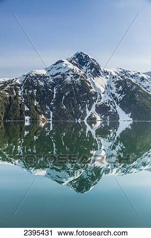 Stock Image - The snow covered Chugach Mountains reflected in the waters of Barry Arm in springtime, Chugach National Forest; Alaska, United States of America. Fotosearch