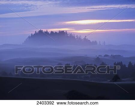 Stock Image - The sun sinks low at sunset with a fog covered landscape; Lakeside, Oregon, United. Fotosearch