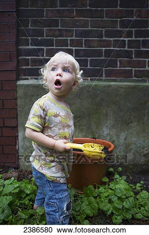 Stock Image - Toddler boy digging with a shovel in the soil in the garden with look of astonishment; Toronto, Ontario, Canada. Fotosearch