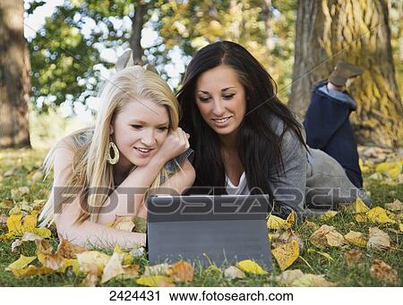 Stock Image - Two friends looking at a tablet in a park in autumn; Edmonton, Alberta, Canada. Fotosearch