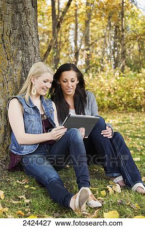 Two friends looking at a tablet in a park in autumn; Edmonton, Alberta, Canada View Large Photo Image Stock Photo - Two friends looking at a tablet in a park in autumn; Edmonton, Alberta, Canada. Fotosearch