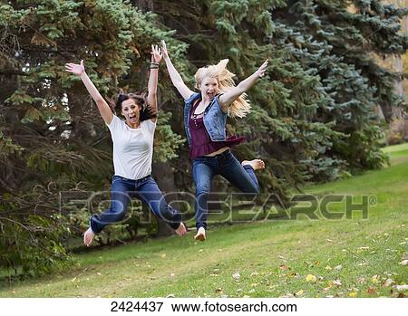 Stock Photo - Two girlfriends leaping for joy in a park in autumn; Edmonton, Alberta, Canada. Fotosearch