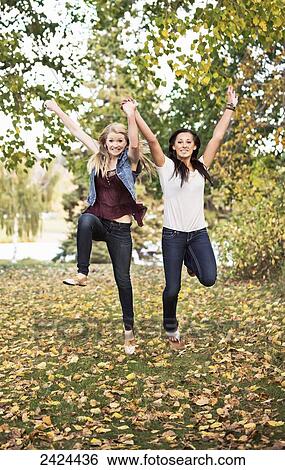 Two girlfriends leaping for joy in a park in autumn; Edmonton, Alberta, Canada View Large Photo Image Stock Photograph - Two girlfriends leaping for joy in a park in autumn; Edmonton, Alberta, Canada. Fotosearch