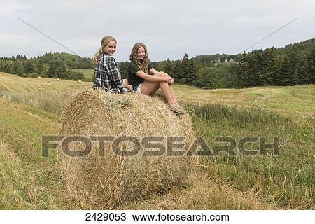 Two girls sit on top of a large hay bale in a field; Kensington, Prince Edward Island, Canada View Large Photo Image Stock Image - Two girls sit on top of a large hay bale in a field; Kensington, Prince Edward Island, Canada. Fotosearch
