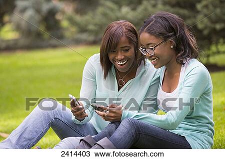 Two sisters using smart phones in the park; Edmonton, Alberta, Canada View Large Photo Image Stock Image - Two sisters using smart phones in the park; Edmonton, Alberta, Canada. Fotosearch