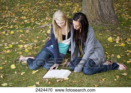 Stock Image - Two teenage girls reading the Bible together in a park; Edmonton, Alberta, Canada. Fotosearch