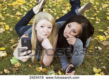 Stock Photograph - Two teenage girls taking a self-portrait with a smart phone in a park in autumn; Edmonton, Alberta, Canada. Fotosearch