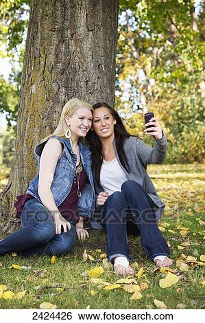 Stock Photograph - Two teenage girls taking a self-portrait with a smart phone in a park in autumn; Edmonton, Alberta, Canada. Fotosearch
