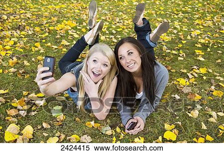 Stock Photography - Two teenage girls taking a self-portrait with a smart phone in a park in autumn; Edmonton, Alberta, Canada. Fotosearch