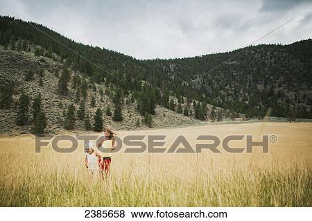 Stock Photo - Two young girls walking in the tall grass of a field; Peachland, British Columbia, Canada. Fotosearch