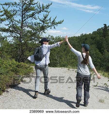 Two young women give each other a high five as they walk down a trail; Manitoba, Canada View Large Photo Image Stock Photo - Two young women give each other a high five as they walk down a trail; Manitoba, Canada. Fotosearch