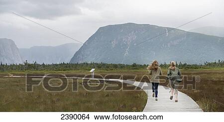 Picture - Two young women walking on a wooden boardwalk at Norris Point; Newfoundland and Labrador, Canada. Fotosearch