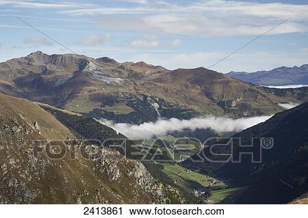 View from top of a mountain looking down a green meadow valley with cloud in the valley and mountain range in the distance; Hintertux, Austria View Large Photo Image Stock Image - View from top of a mountain looking down a green meadow valley with cloud in the valley and mountain range in the distance; Hintertux, Austria. Fotosearch