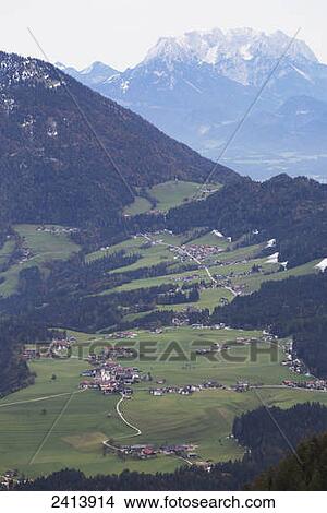 Picture - View of an alpine village with green meadows, rolling hills and trees in autumn and snow capped mountains in the distance; Brandenberg, Austria. Fotosearch