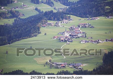 Stock Image - View of an alpine village with green meadows, rolling hills and trees in autumn; Brandenberg, Austria. Fotosearch