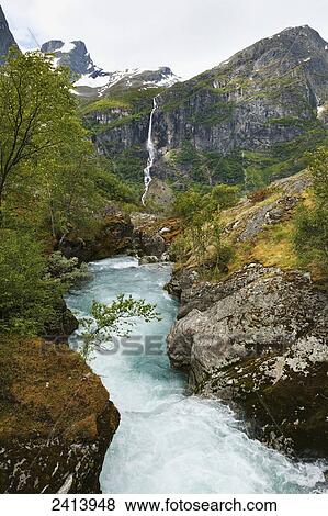 Water rushing in a river in a valley between the mountains with a waterfall on a steep cliff in the distance; Olden, Norway View Large Photo Image Stock Photo - Water rushing in a river in a valley between the mountains with a waterfall on a steep cliff in the distance; Olden, Norway. Fotosearch