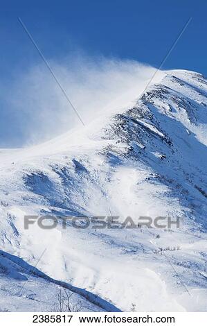 Stock Photo - Wind driven snow blows off the peak of a snow covered mountain in wintertime, Dutch hills; Petersville, Alaska, United States of America. Fotosearch