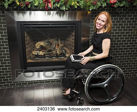 Woman in a wheelchair by the fireplace holding a tablet; Edmonton, Alberta, Canada View Large Photo Image Stock Photograph - Woman in a wheelchair by the fireplace holding a tablet; Edmonton, Alberta, Canada. Fotosearch