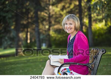Stock Image - Woman reading her Bible on a park bench; Edmonton, Alberta, Canada. Fotosearch