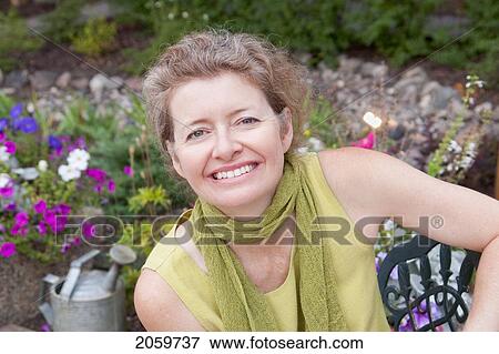 Stock Photo - Woman Seated On Metal Seat In Flower Garden, Manitoba, Canada. Fotosearch