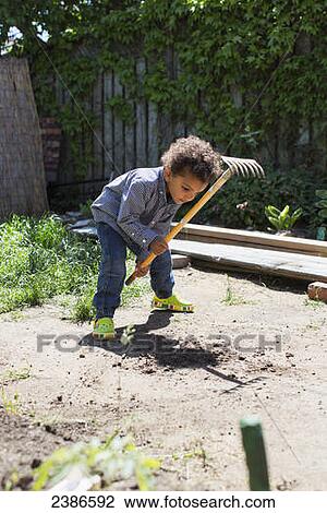 Stock Image - Young boy digging with rake in the garden; Toronto, Ontario, Canada. Fotosearch