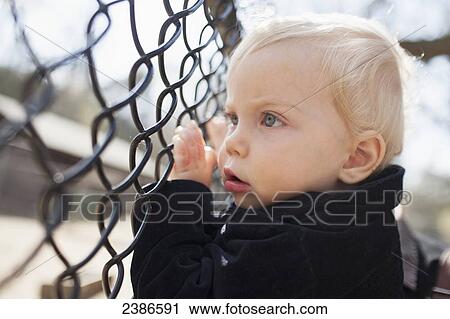 Stock Image - Young boy looks through the fence at park; Toronto, Ontario, Canada. Fotosearch