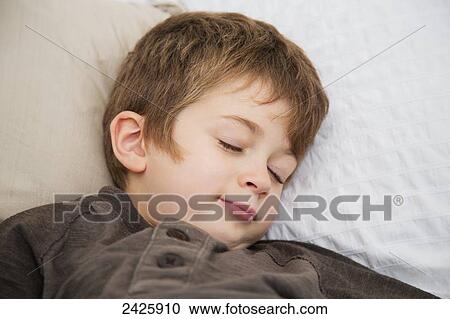 Stock Image - Young boy pretending to be asleep in bed; Langley, British Columbia, Canada. Fotosearch