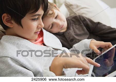Stock Photograph - Young boys playing with a tablet in bed; Langley, British Columbia, Canada. Fotosearch