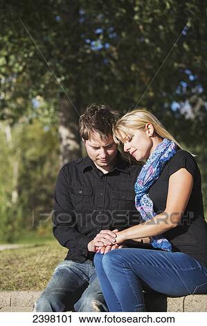 Stock Image - Young couple praying together in a park; Edmonton, Alberta, Canada. Fotosearch